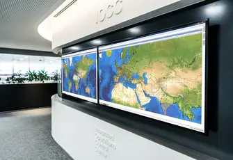 Large display screens in an Integrated Operations Control Center showing global maps for flight operations monitoring and control