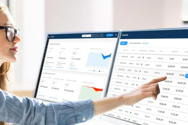 Person working on two monitors displaying financial and analytical data in a modern office setting.