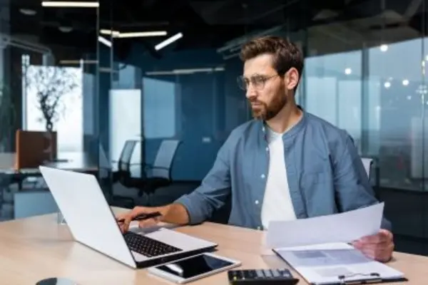 Person working at a desk with a laptop, documents, and a calculator in a modern office.