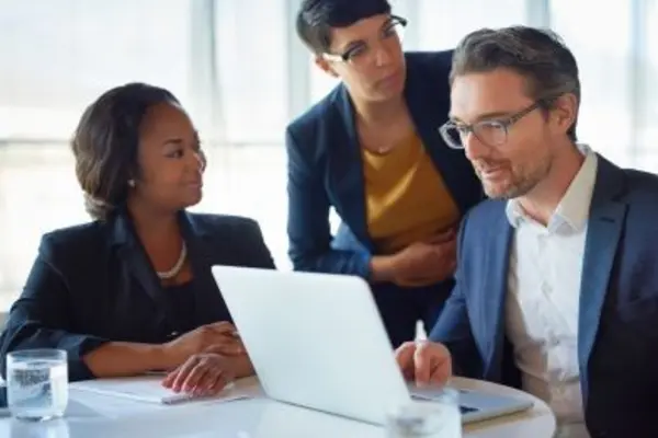 Three people working together on a laptop during a meeting.