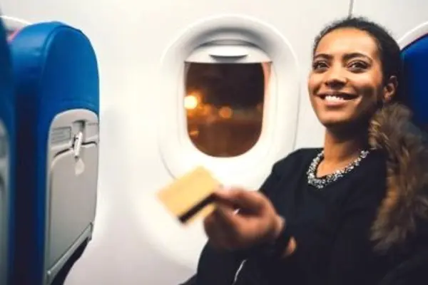 Person holding a credit card during a flight, seated by the window.