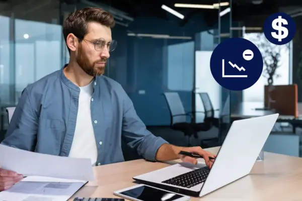 Person working on a laptop with documents on the desk, financial icons and charts in the background.