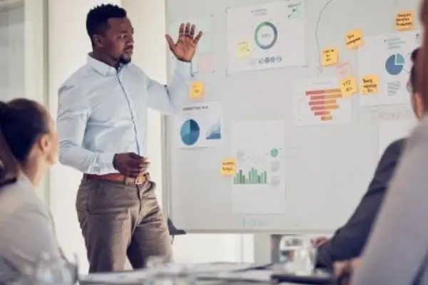 Person presenting charts and statistics on a whiteboard during a meeting.