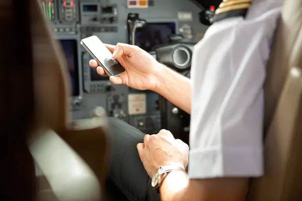 Pilot im Cockpit hält ein Smartphone in der Hand