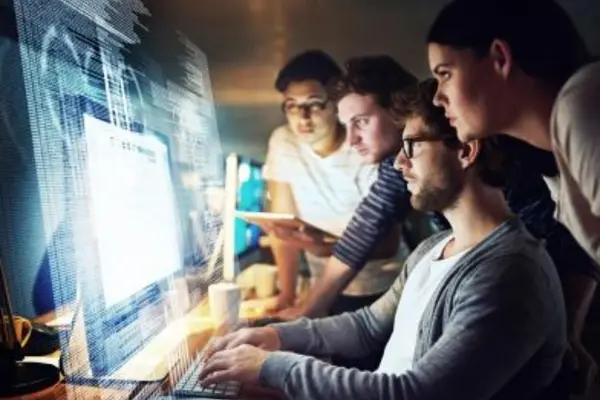 Team collaborating on computer with programming code in office