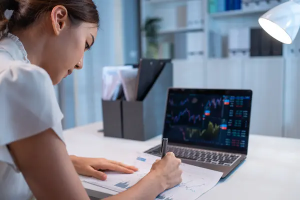 Laptop showing charts, person writing on a document.