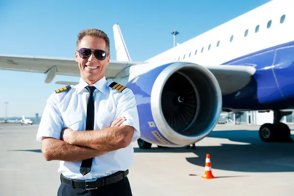 Pilot standing with crossed arms in front of an aircraft on the tarmac