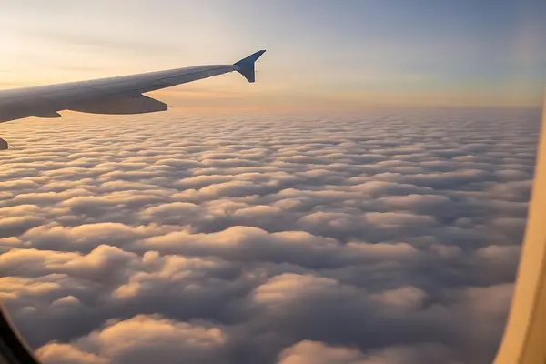  Blick aus dem Flugzeugfenster auf eine Wolkendecke bei Sonnenaufgang