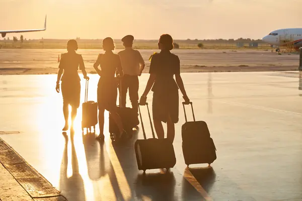 Crew members walk across the apron with luggage toward an aircraft at sunset