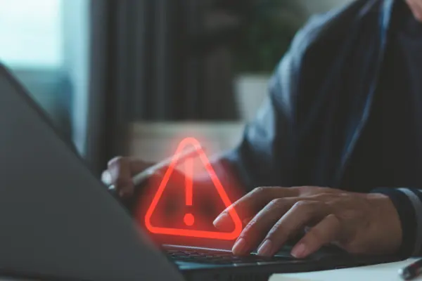 Cyber security warning concept. Businessman typing on laptop, showing alert symbol and data risk notification. Cybersecurity, system error, data protection, hacking prevention, IT security services.