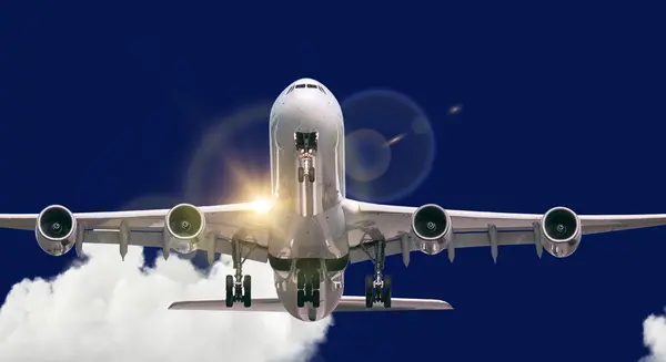 A large passenger airplane on final approach, photographed from the front with extended landing gear and four engines, against a deep blue sky and clouds in the background.