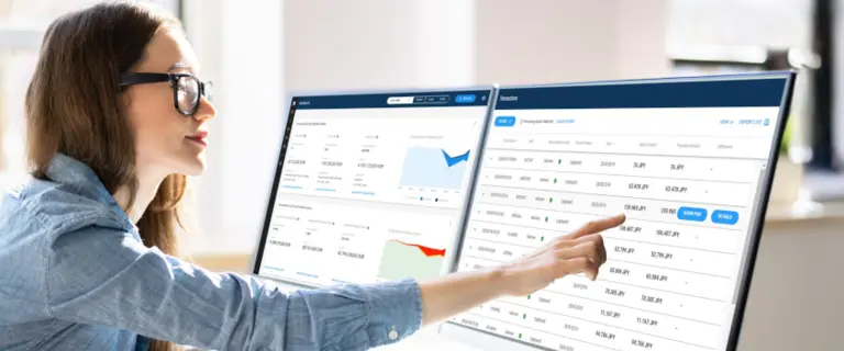 Person working on two monitors displaying financial and analytical data in a modern office setting.
