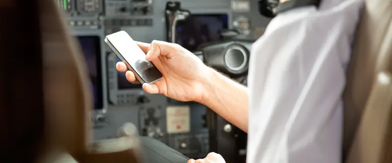 Pilot im Cockpit hält ein Smartphone in der Hand