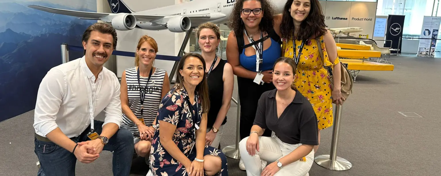 A part of the global IT project team stands in front of a Lufthansa model airplane.