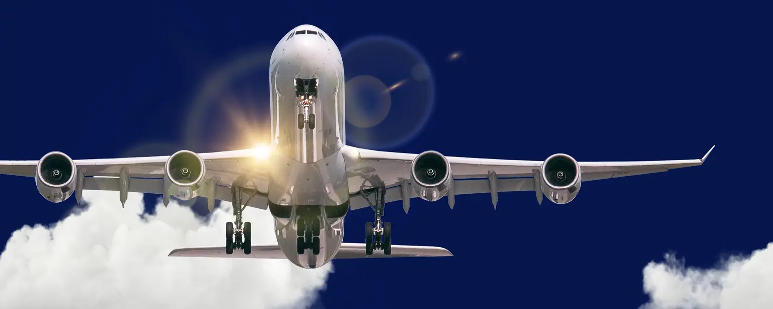 A large passenger airplane on final approach, photographed from the front with extended landing gear and four engines, against a deep blue sky and clouds in the background.