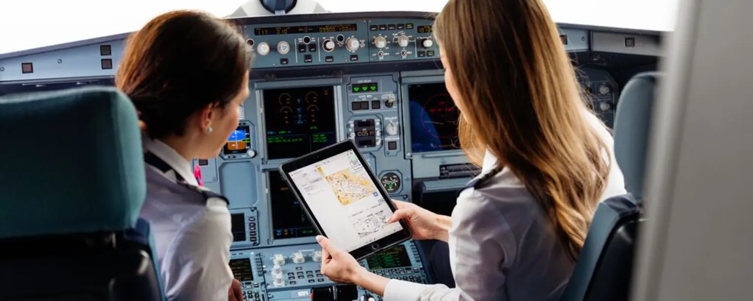 two female pilots in airplane cockpit looking at iPad screen