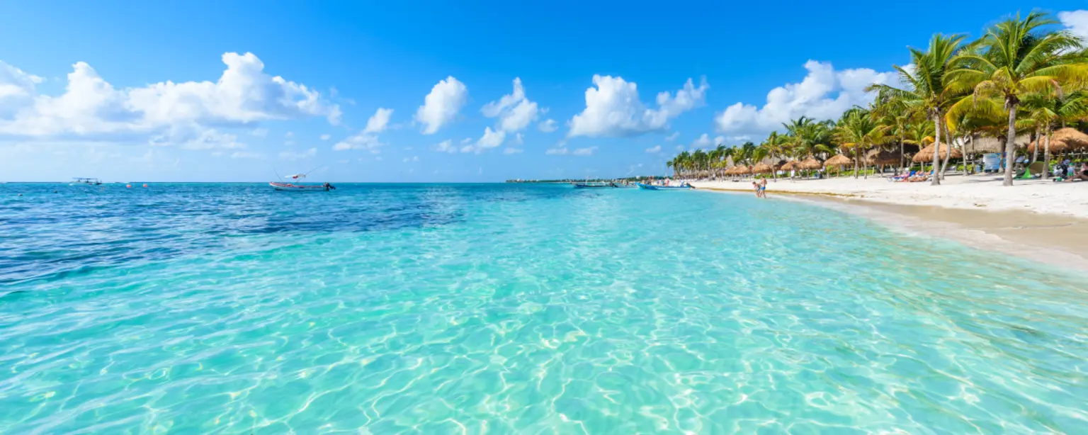Das türkisfarbene Meer entlang eines tropischen Sandstrandes mit Palmen und einem strahlend blauen Himmel